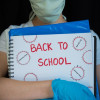 Student wearing gloves and mask, holding "Back to School" notebook