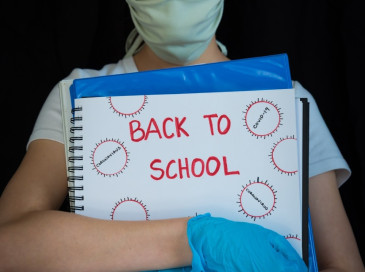 Student wearing gloves and mask, holding "Back to School" notebook